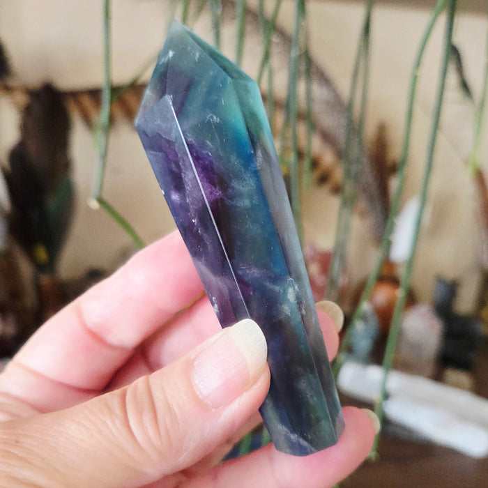 A hand holding a polished Fluorite sceptre with a visible multicolored pattern.