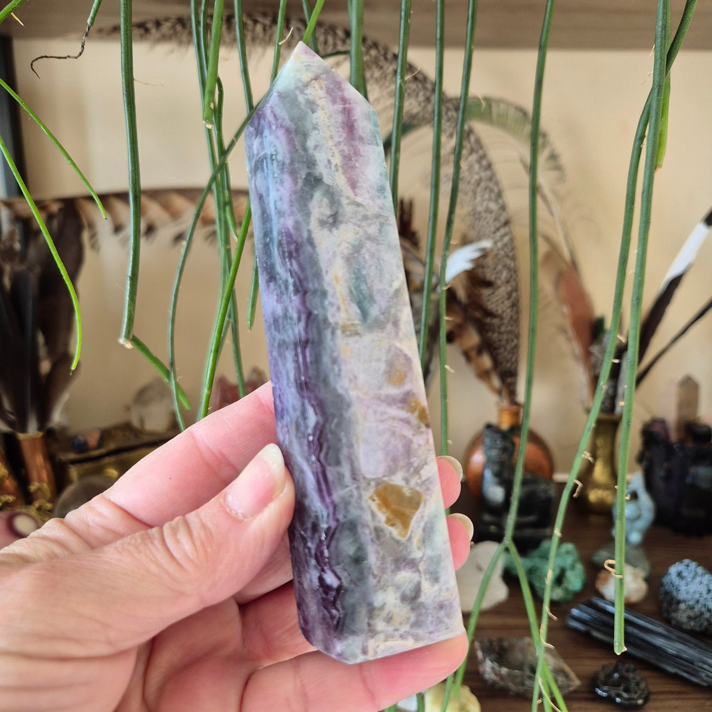 A hand holding a fluorite tower with a colorful, layered appearance, surrounded by various decorative items.