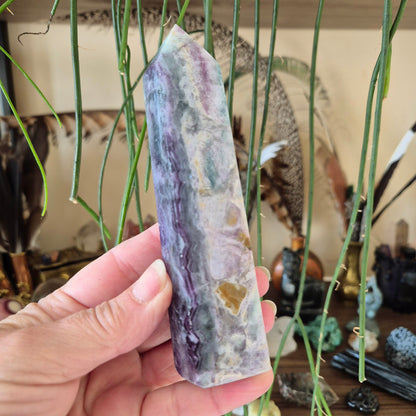 A hand holding a fluorite tower with a colorful, layered appearance, surrounded by various decorative items.