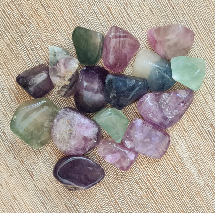 A collection of polished Fluorite stones in various shades of purple, green, and gray, displayed on a wooden surface.