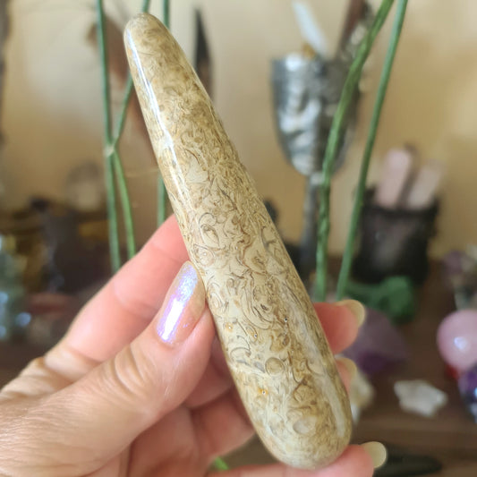 A beige crystal wand with a floral pattern, held in a person's hand, with various decorative items in the background.