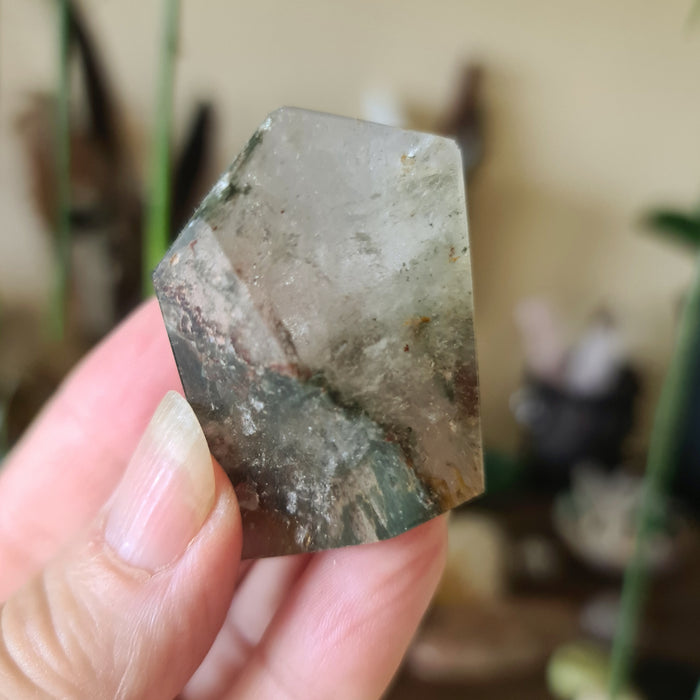 A polished piece of garden quartz crystal with natural variations in color and pattern, held in a person's hand.