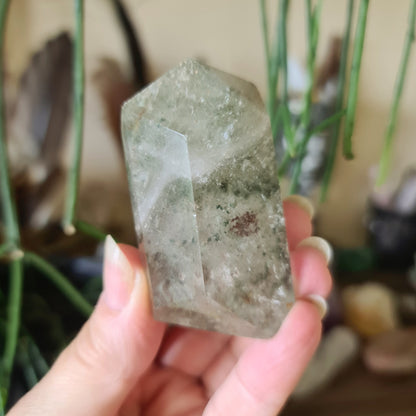 A polished green quartz crystal held in a person's hand, with natural variations in color and texture.