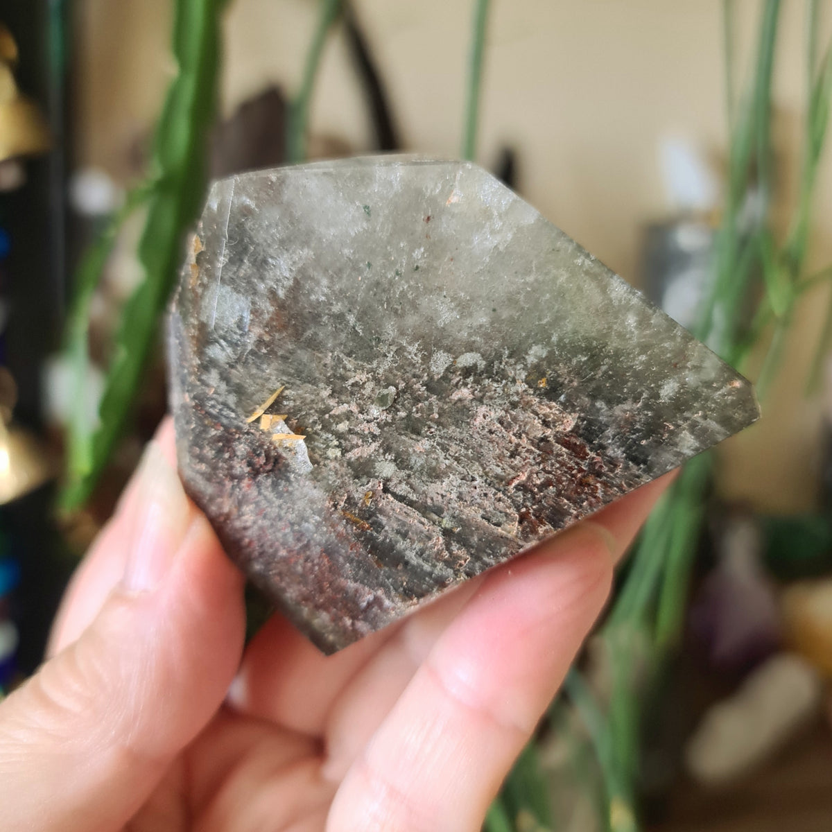 A polished piece of garden quartz crystal held in a person's hand, with natural variations in color and pattern.