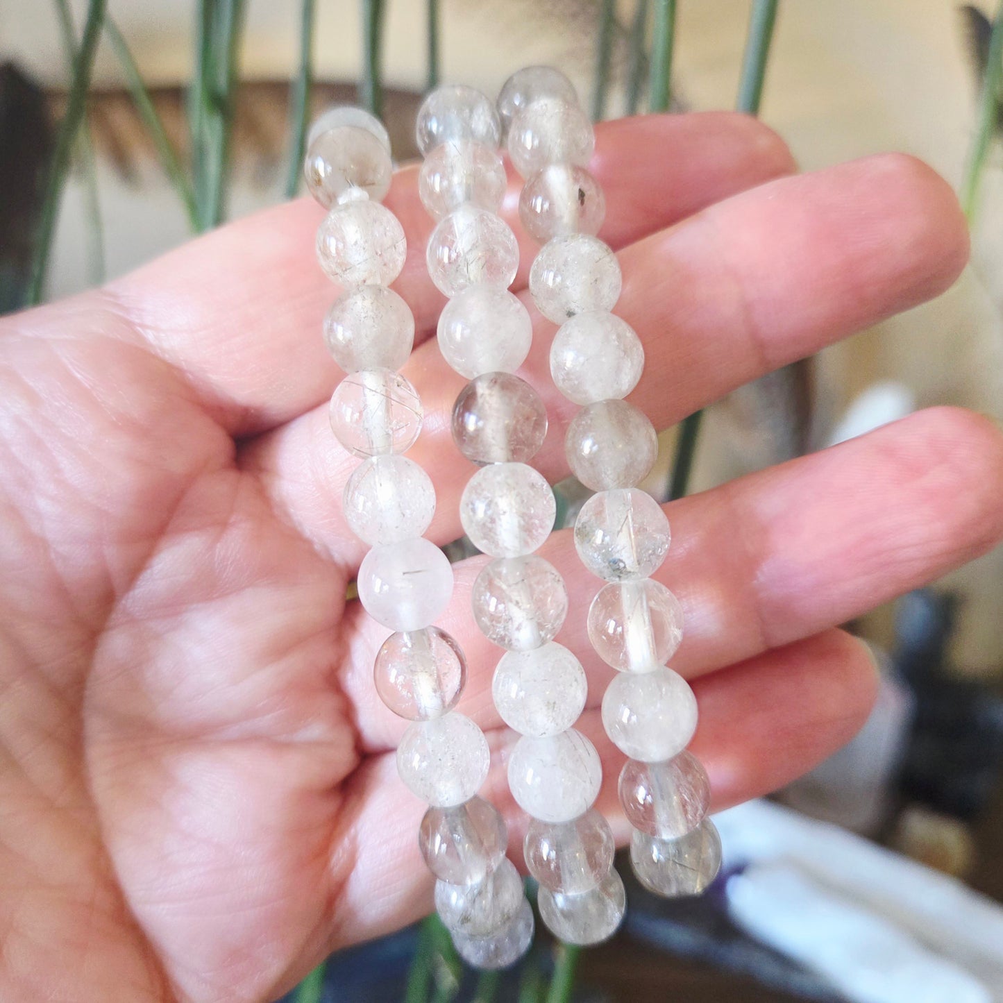 A hand holding a bracelet made of clear round beads.
