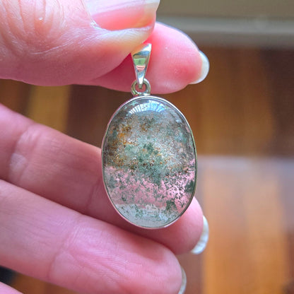 Hand holding a silver pendant with an oval stone