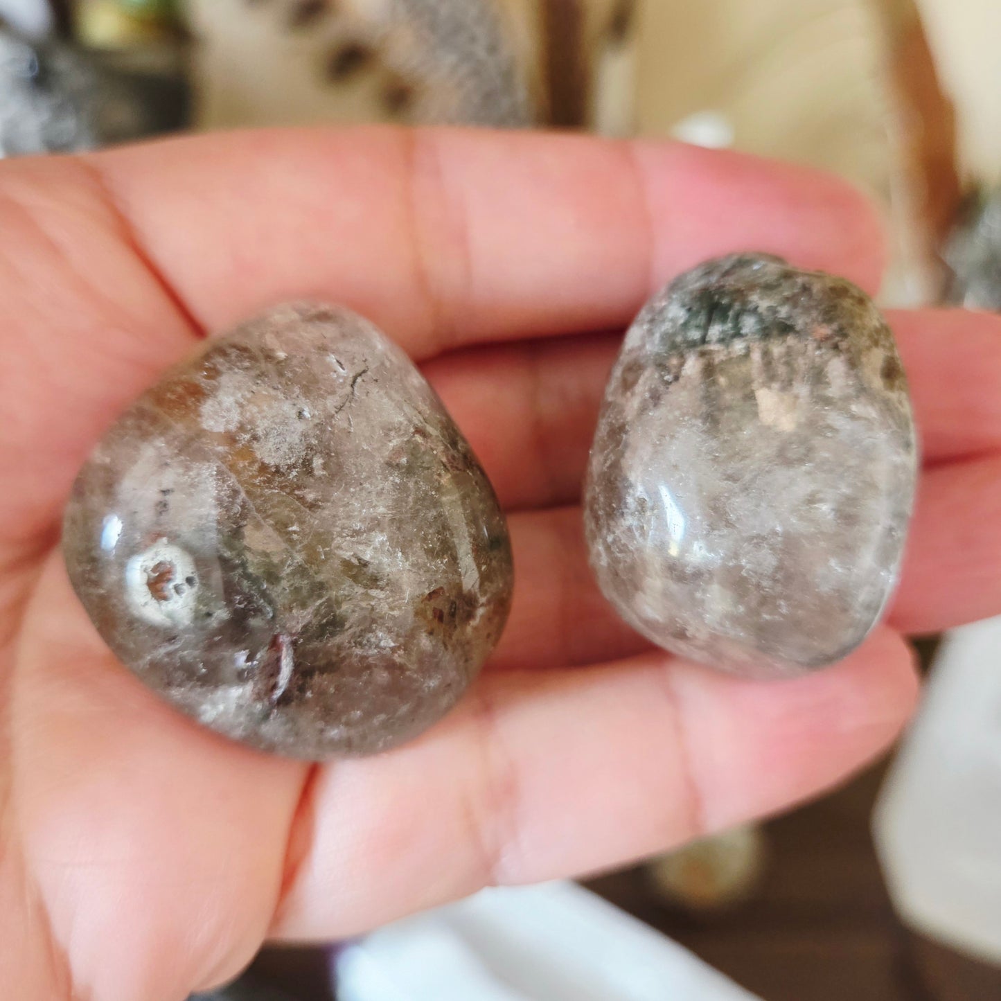 Two polished Garden Quartz Tumbles held in a person's hand, with a blurred background.