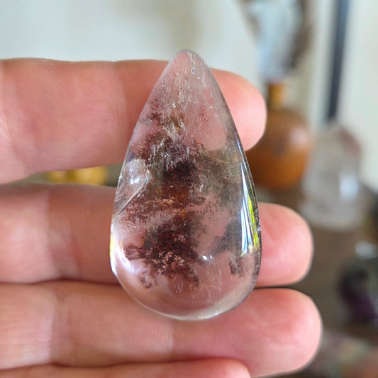 Teardrop-shaped crystal held between fingers with a blurred background