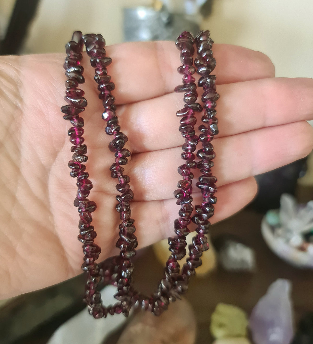 A hand holding a brown garnet chip necklace with red and dark brown stones.