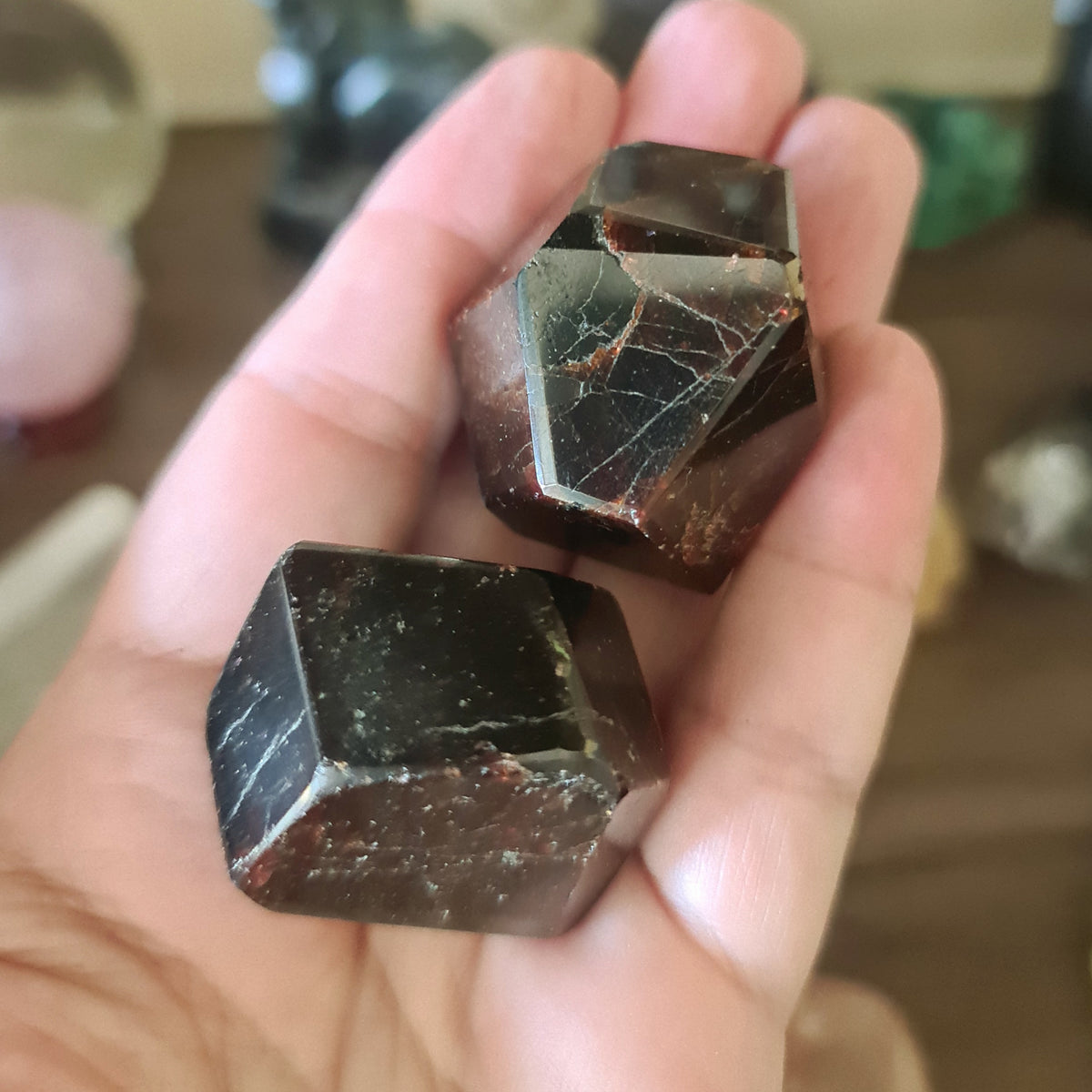 A person holding a polished garnet crystal, which is red with a blackish tint and has a marbled appearance.