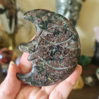 A bright red garnet crystal shaped like a crescent moon, held in a person's hand.
