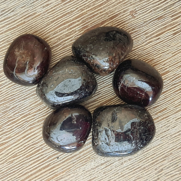 large dark red crystal tumbles on a timber background