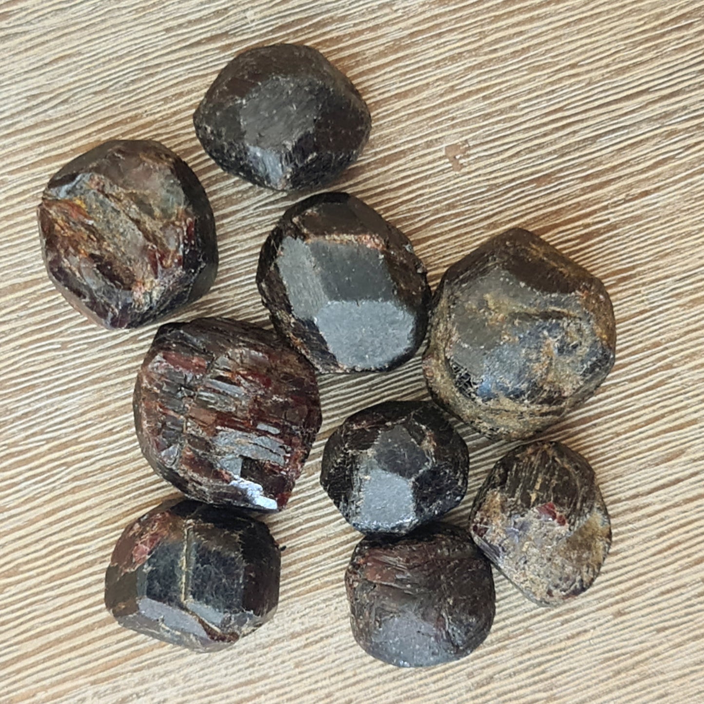A collection of raw, unpolished garnet tumble stones displayed on a wooden surface.
