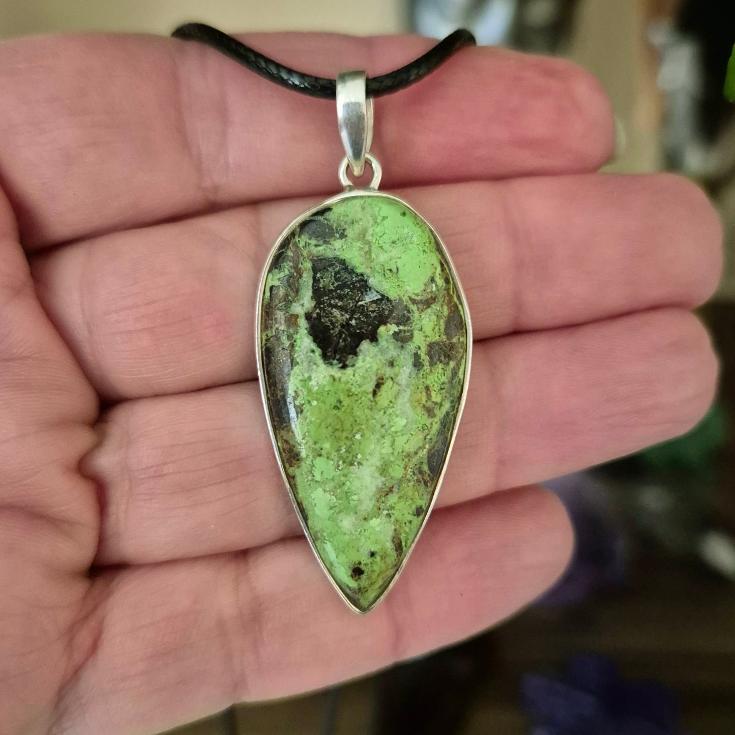 A sterling silver pendant with a teardrop-shaped Gaspeite crystal attached to a black necklace.