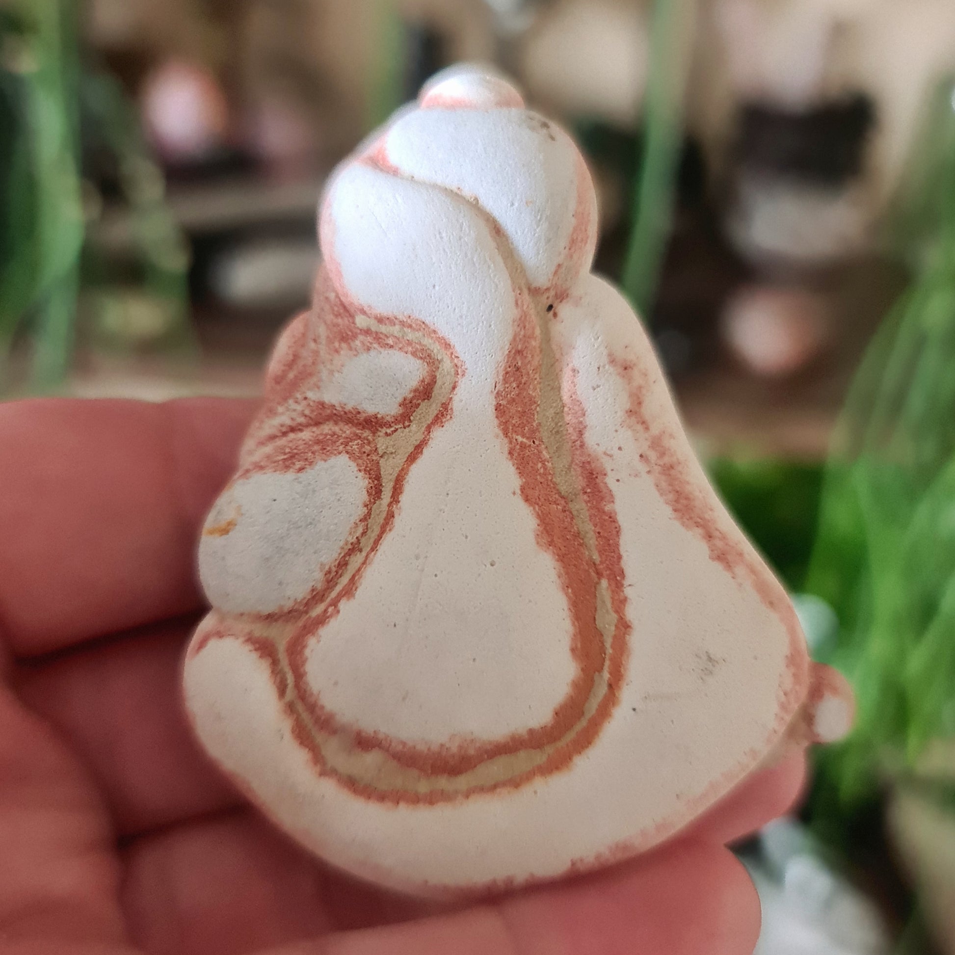 A hand holding a beige and red patterned crystal stone, resembling a shamanic figure or spirit being.