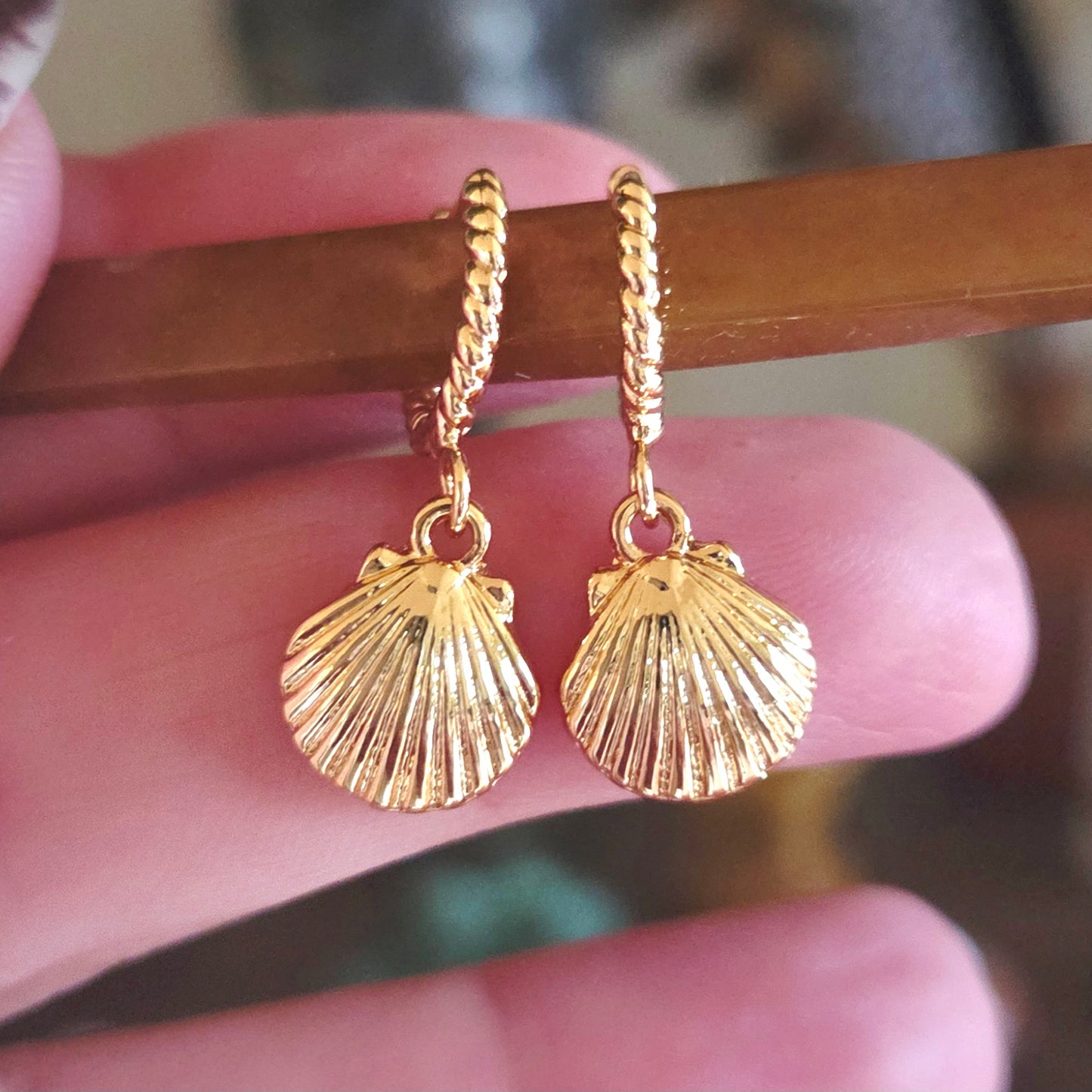 Gold shell-shaped earrings held between fingers with a blurred background