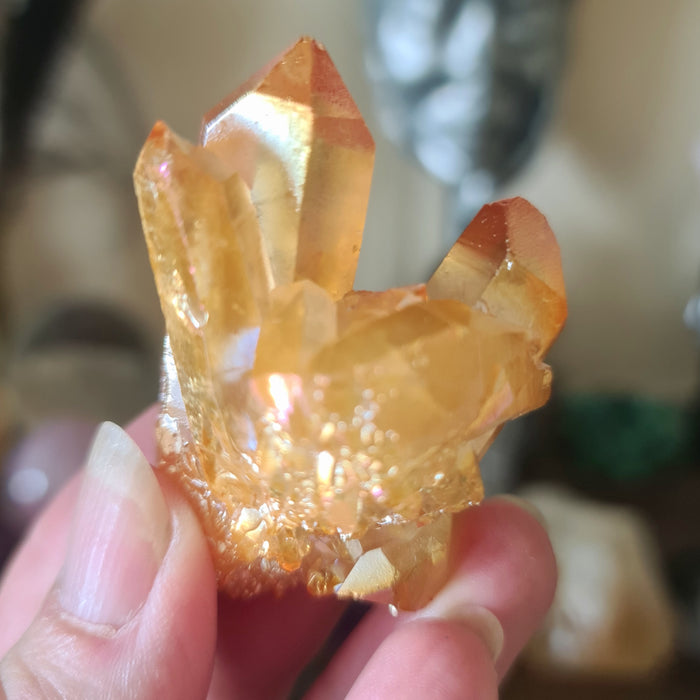 A hand holding a polished, golden-colored crystal quartz cluster.
