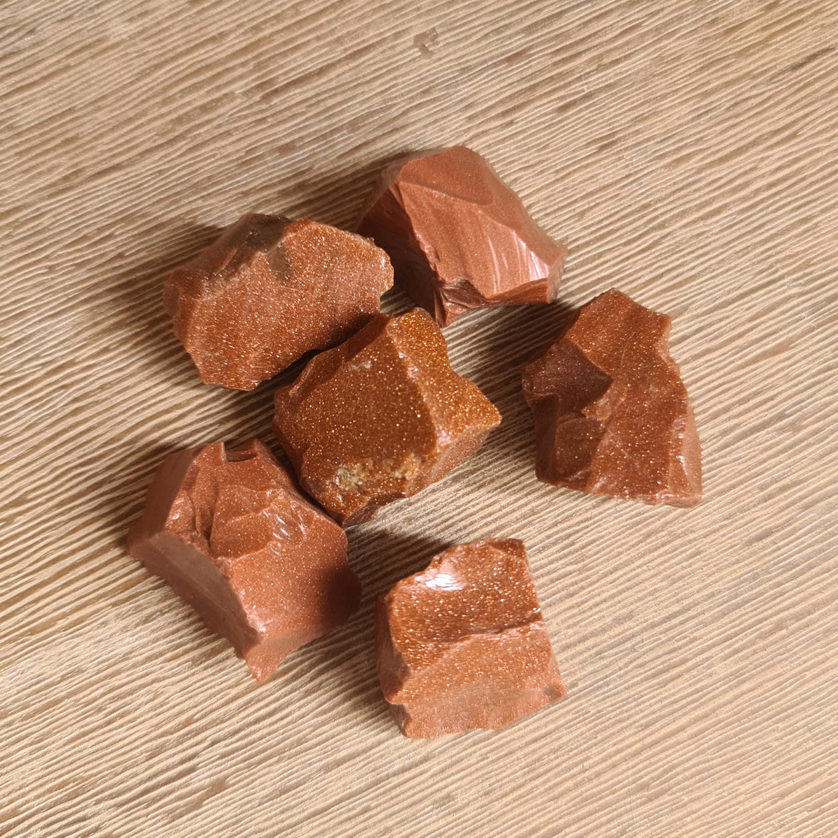 A collection of raw, unpolished goldstone beads with a natural brown to reddish color, displayed on a wooden surface.