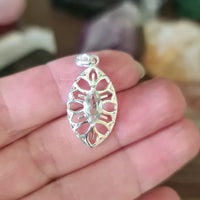 A sterling silver pendant with a green amethyst gemstone set in it, held between fingers.