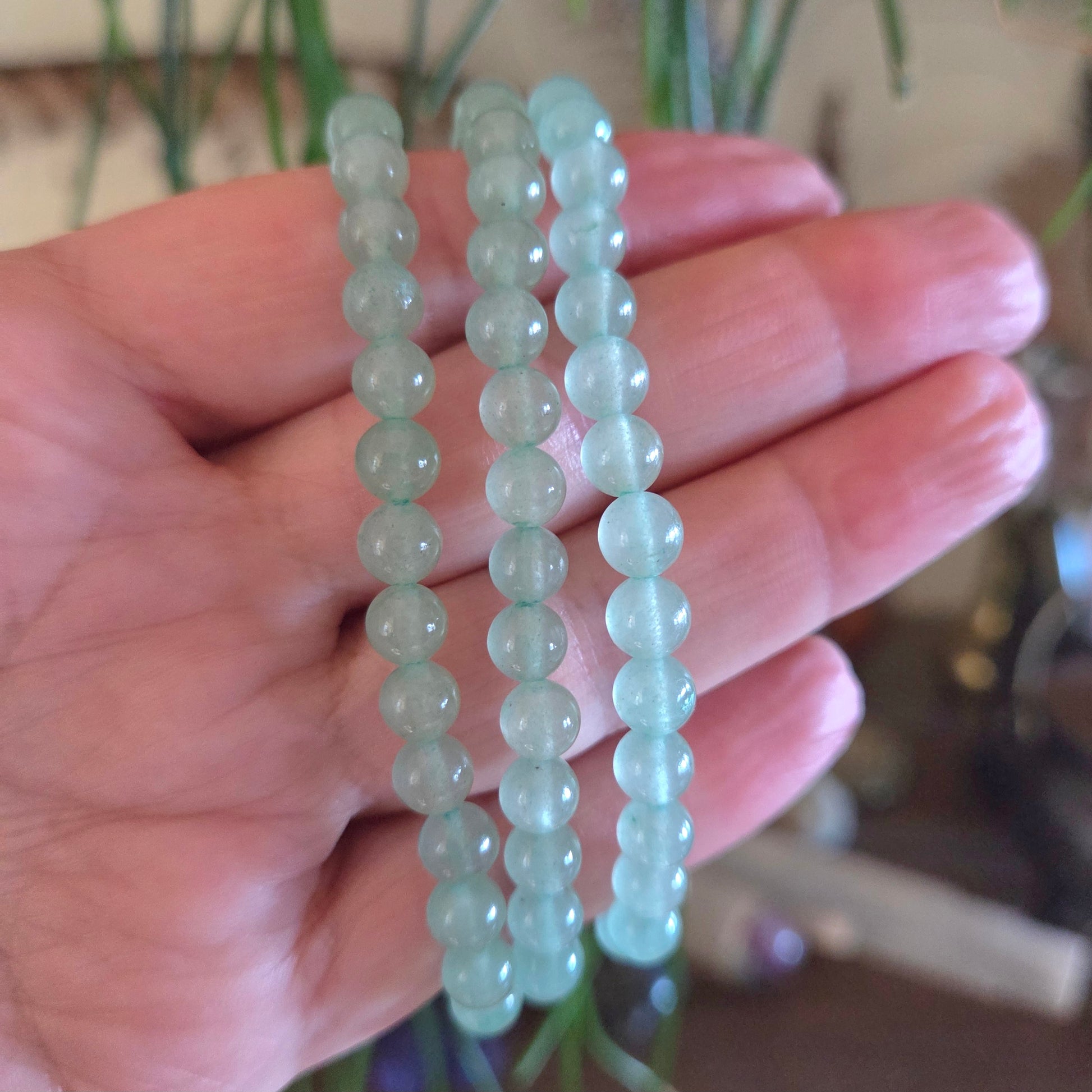 A hand holding a green aventurine bracelet with round beads.