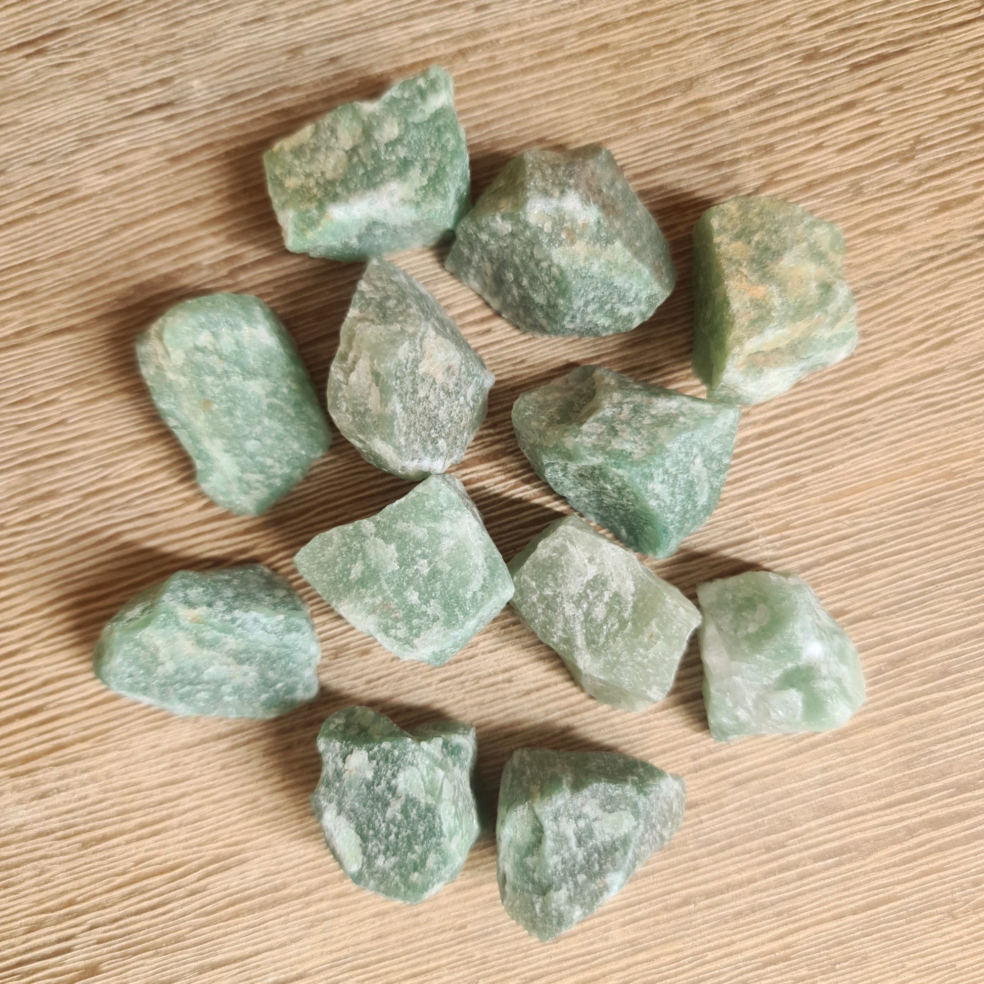 A collection of raw green aventurine crystals on a wooden surface.