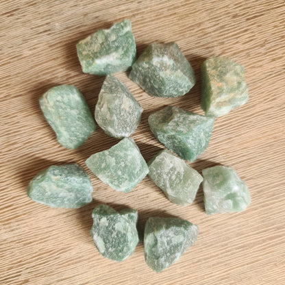 A collection of raw green aventurine crystals on a wooden surface.