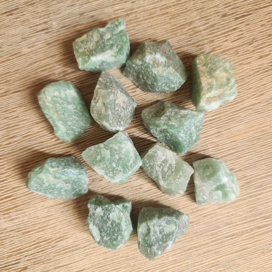 A collection of raw green aventurine crystals on a wooden surface.