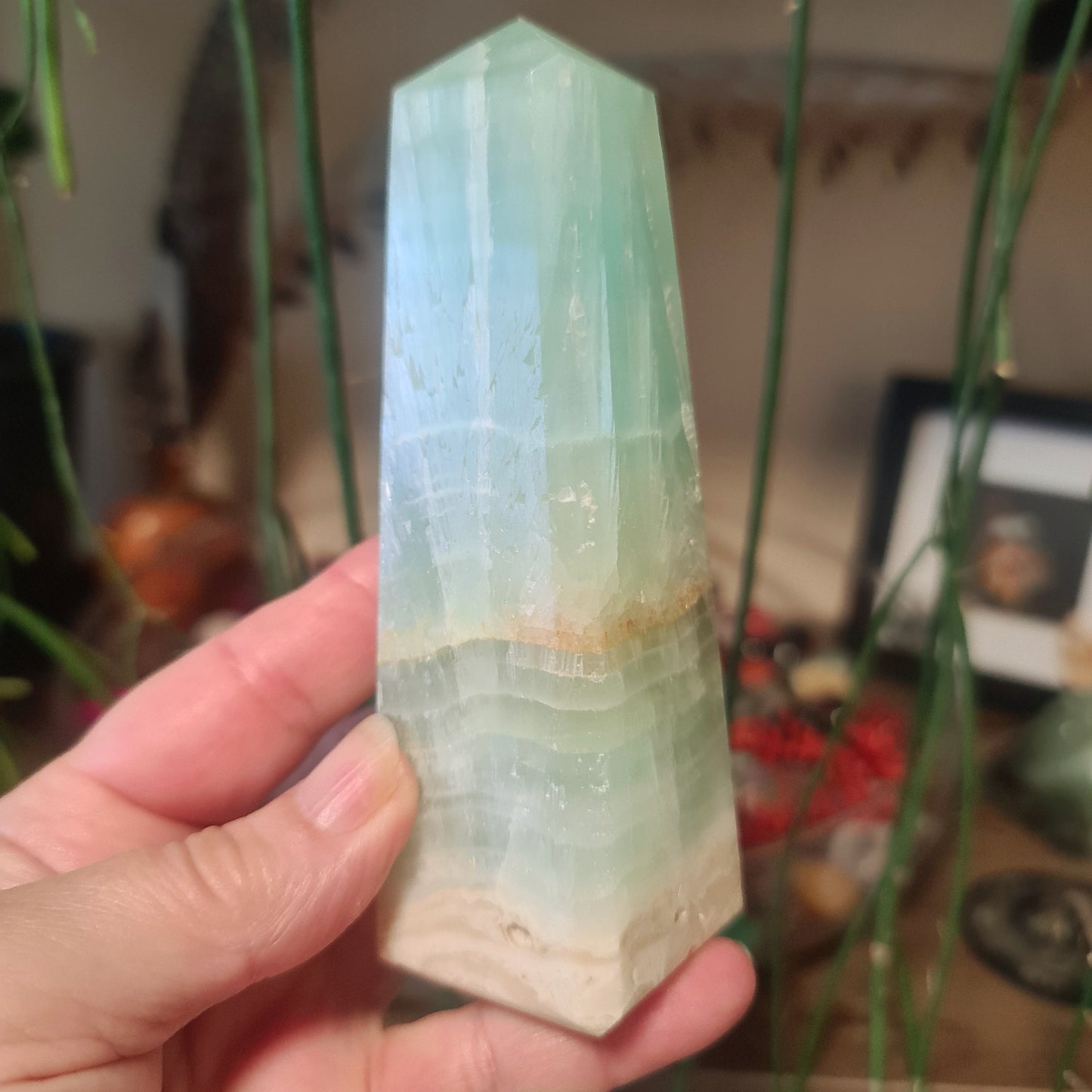A green calcite crystal in a tower shape with a person's hand for scale, held in a home environment.