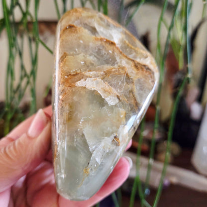 A freeform Green Onyx gemstone held in a person's hand, with a translucent appearance and natural color variations.