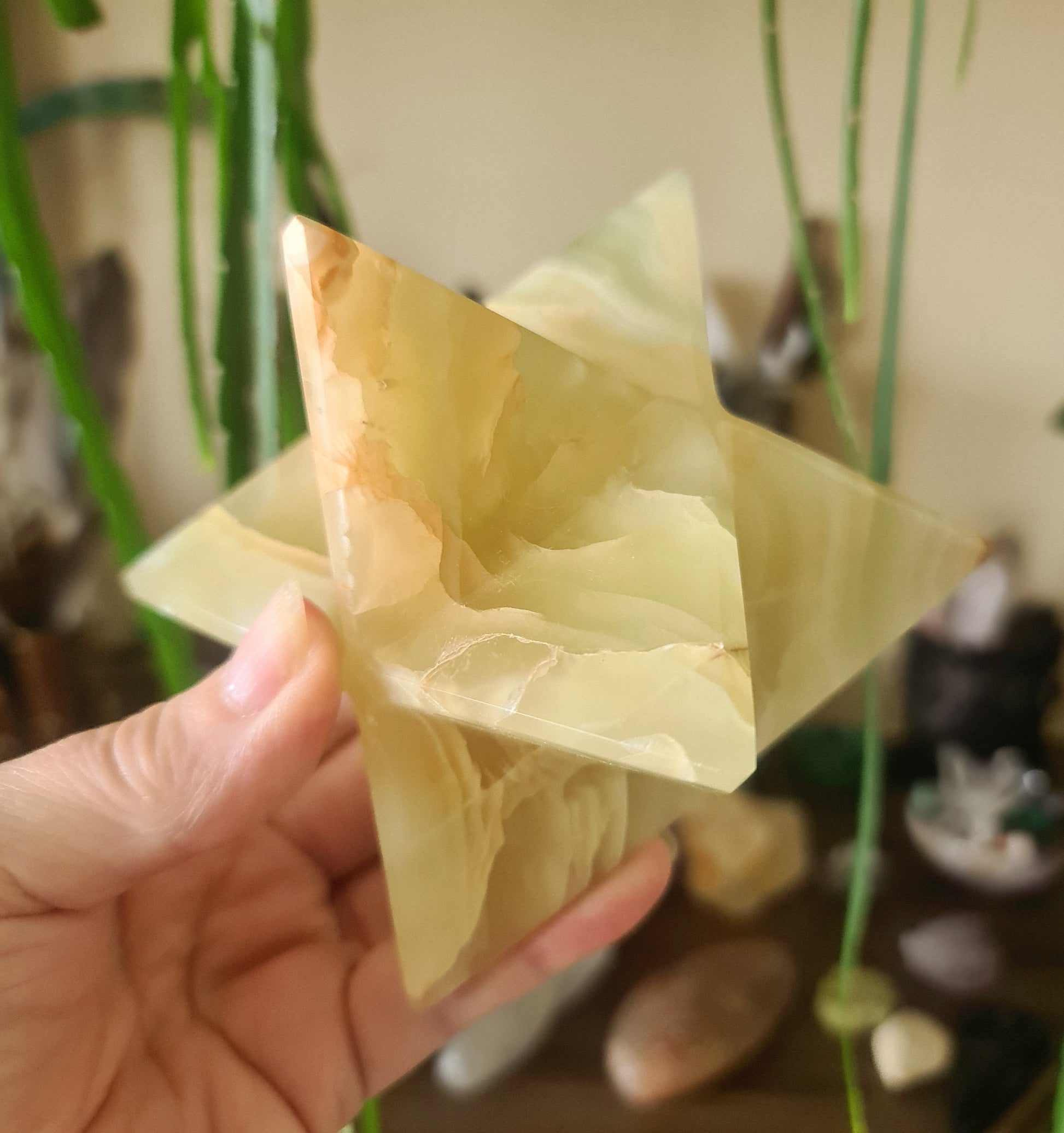 A green onyx merkaba, held in a person's hand, with a triangular pyramidal shape and a polished, smooth surface.