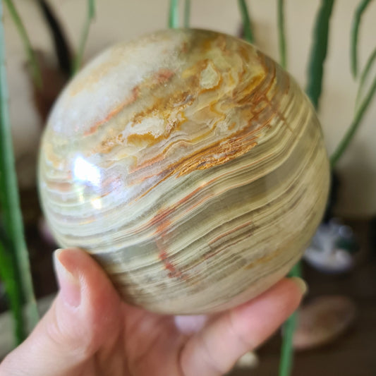 A hand holding a large green onyx sphere with natural color variations.