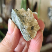 A person holding a green tourmaline chunk with a rough, natural surface.