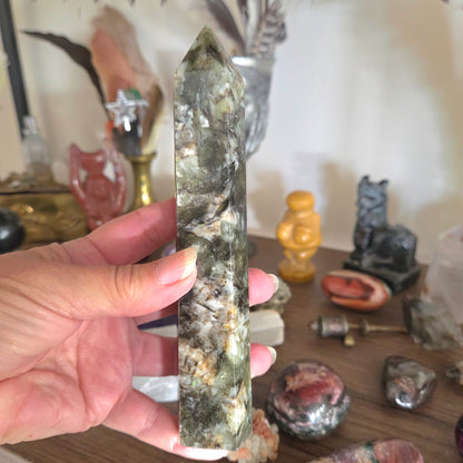 Hand holding a green crystal wand with a blurred background of decorative items.