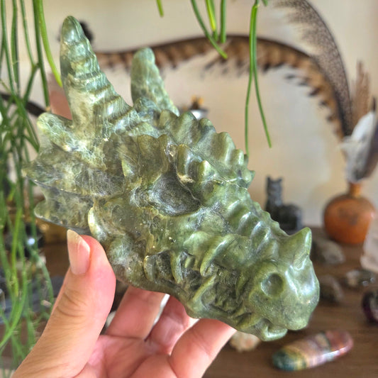 Hand holding a green stone dragon sculpture with a blurred background