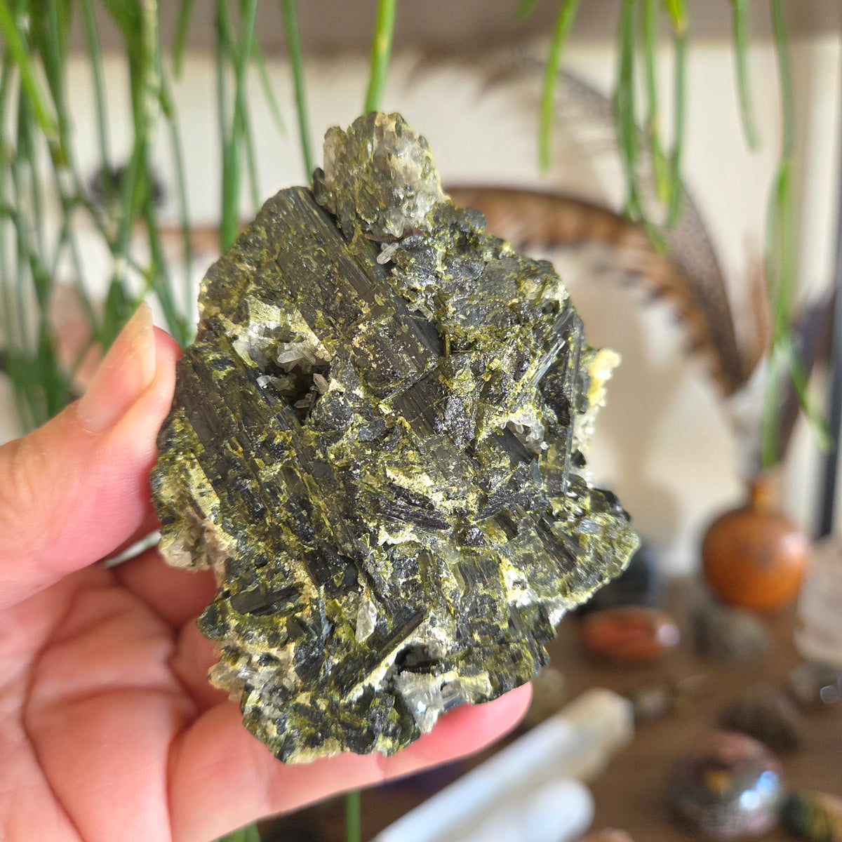 Hand holding a large green mineral crystal with a blurred indoor setting