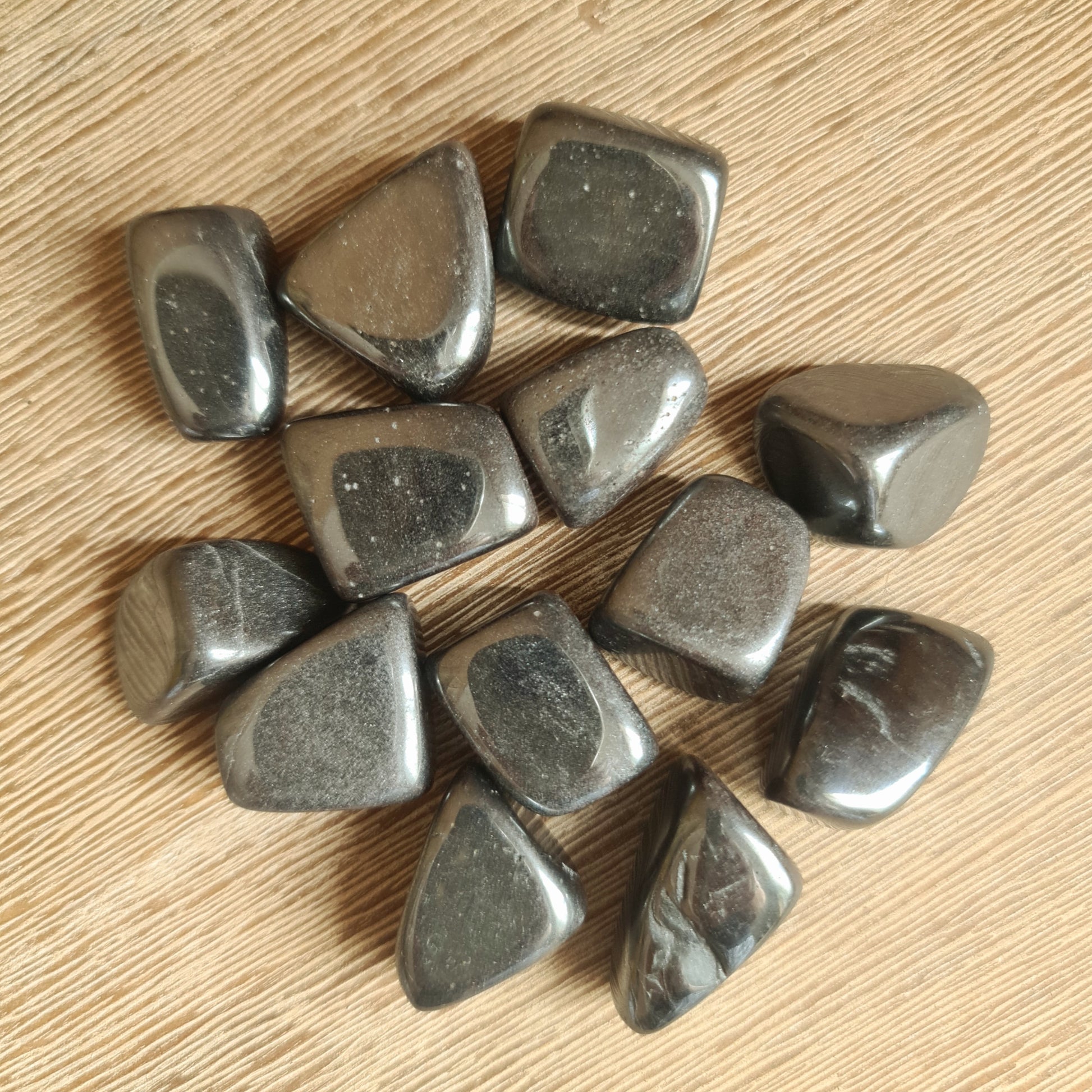 A collection of polished hematite stones with a metallic sheen, displayed on a wooden surface.