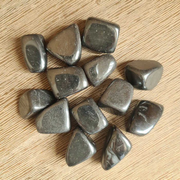 A collection of polished hematite stones with a metallic sheen, displayed on a wooden surface.