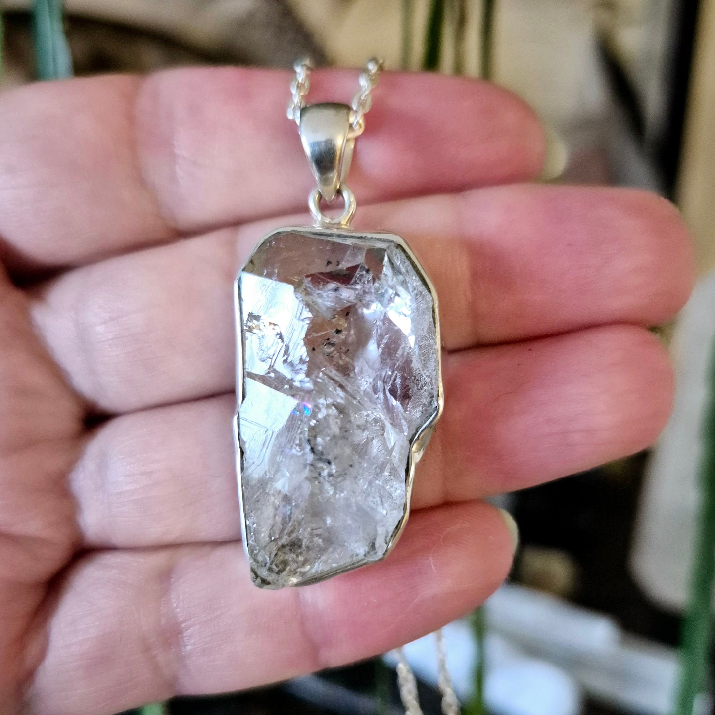 A hand holding a silver Herkimer diamond pendant with a chain, showcasing the crystal's clarity and inclusions.