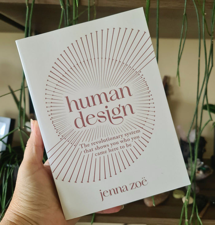 A hand holding a book titled 'Human Design' by Jenna Zoe, with a minimalist design featuring a sunburst and the author's name.