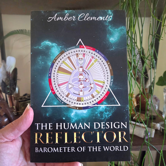 Book titled 'The Human Design Reflector' by Amber Clements held in front of a blurred indoor background.