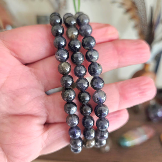Three black beaded bracelets held in a hand with a blurred background