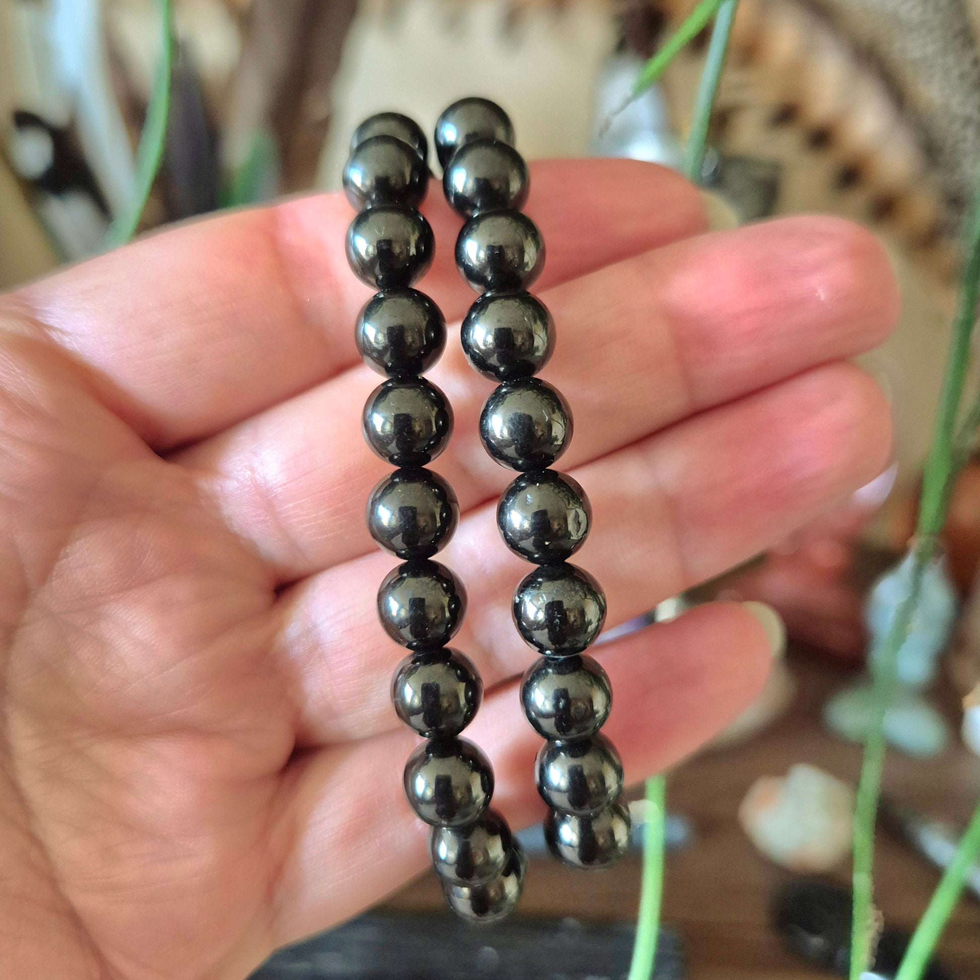A close-up image of a hand holding a black jet bracelet with polished beads.