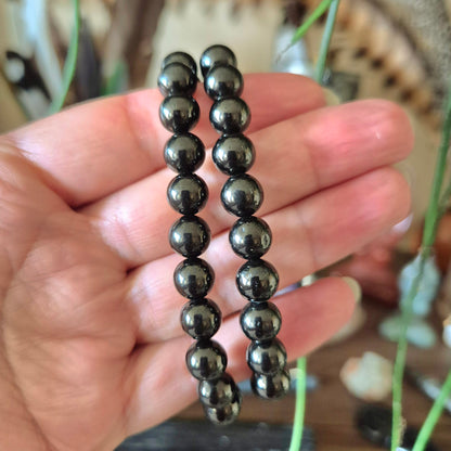 A close-up image of a hand holding a black jet bracelet with polished beads.