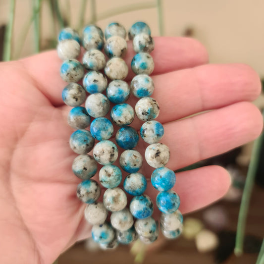 A hand holding a beaded bracelet with blue and white round beads.