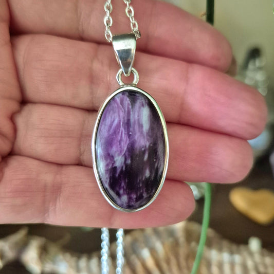A silver-colored pendant featuring a purple variety of Clinochlore gemstone held in a hand.