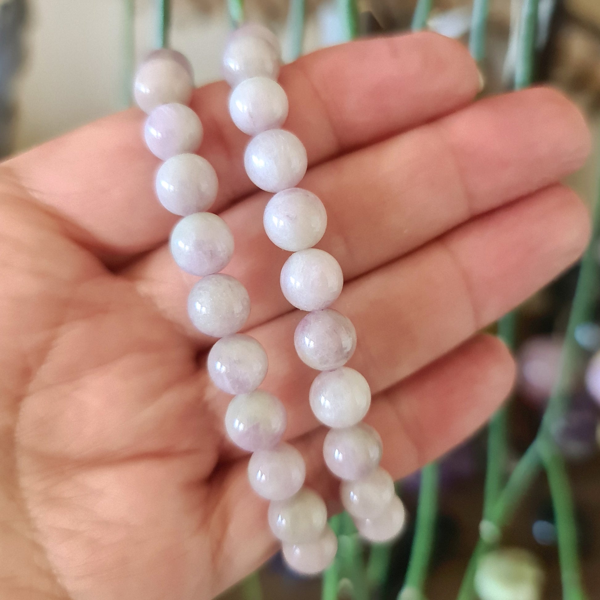 A hand holding a kunzite bracelet with multiple beads featuring a smooth, polished surface.