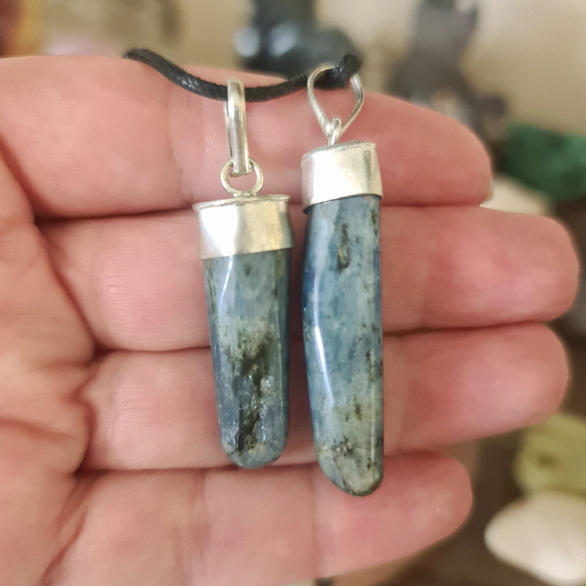 A hand holding a blue kyanite pendant with a silver cap and chain.