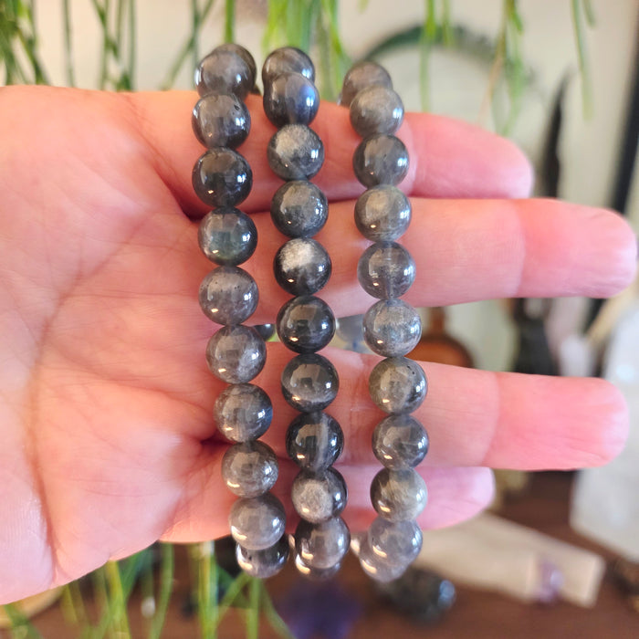 Two gray beaded bracelets held in a hand with a blurred background