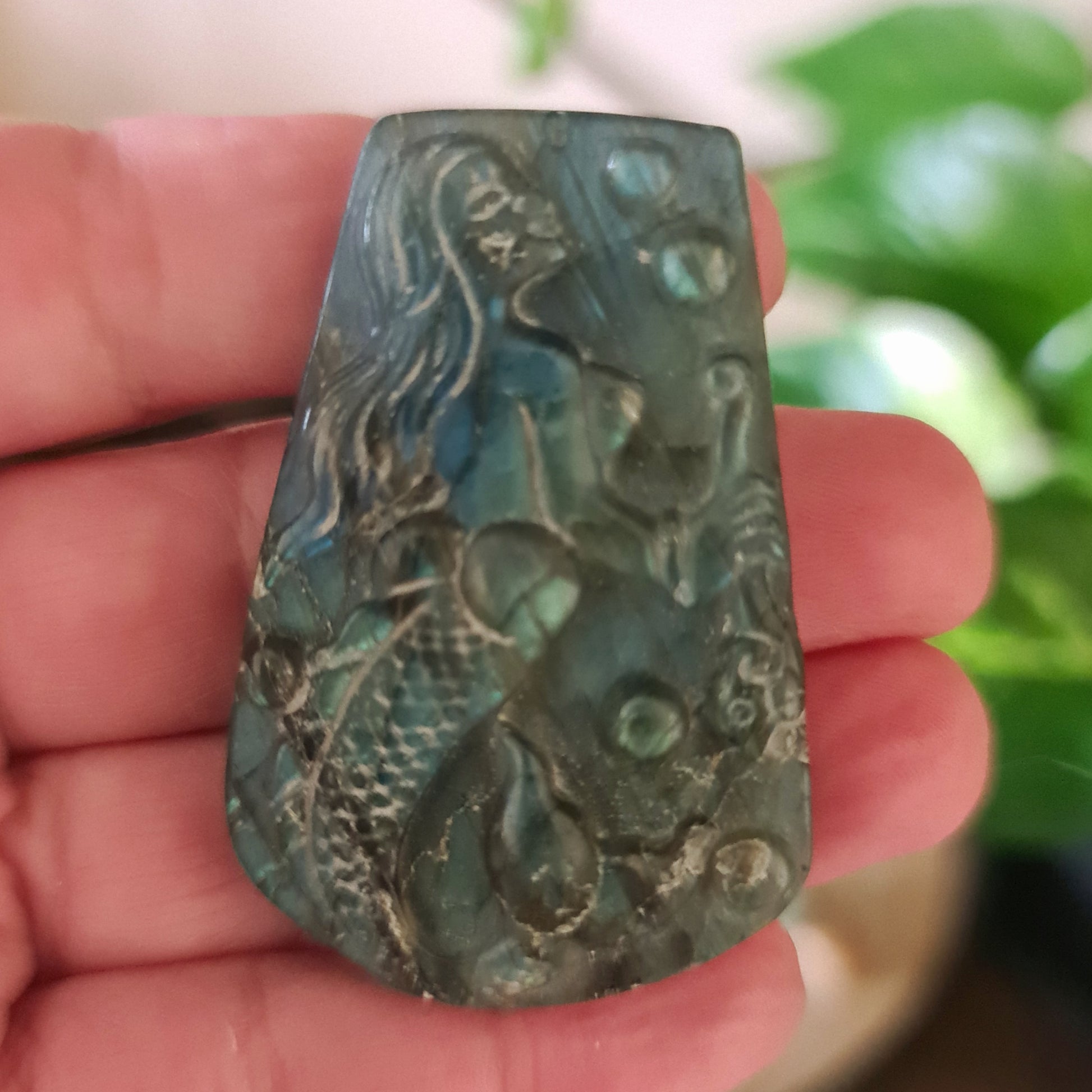 A palm-sized carved tile with a blue and gray mermaid design, held in a person's hand.