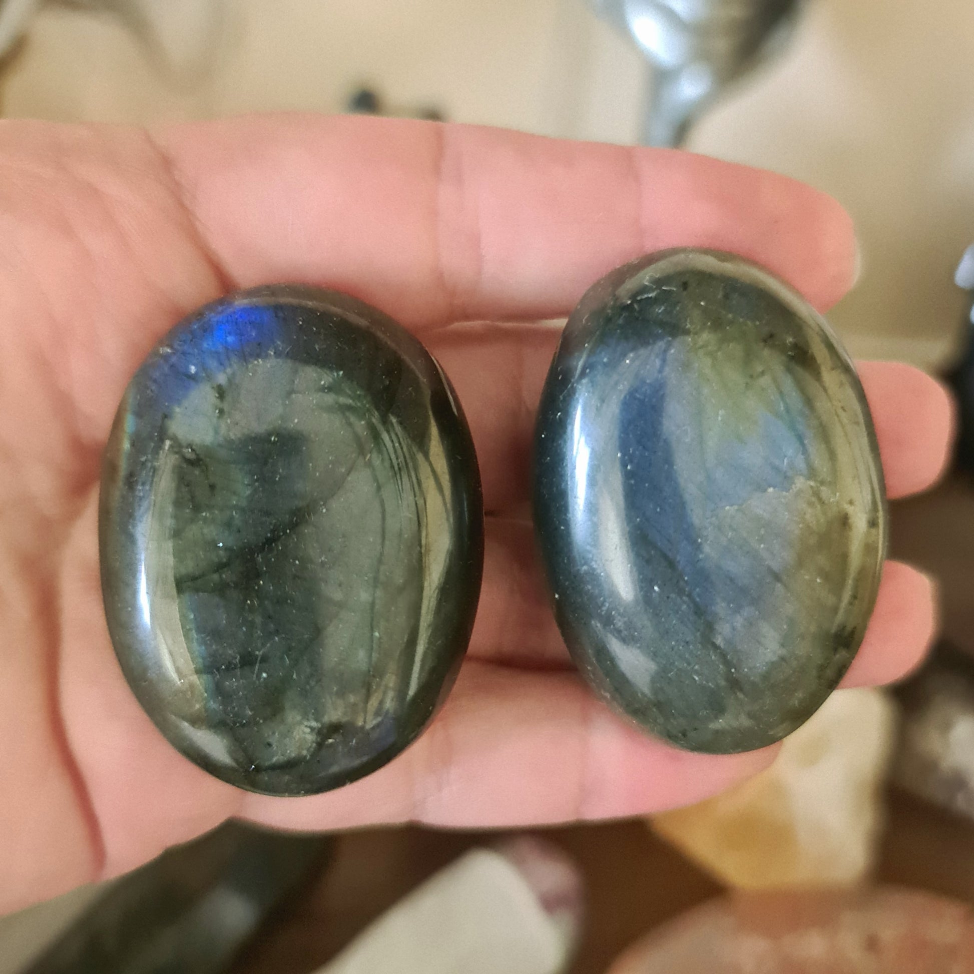 Two polished labradorite stones with a greenish-blue and blue sheen, held in a person's hand.